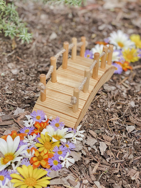 Miniature wooden bridge surrounded by colorful flowers on a natural ground surface