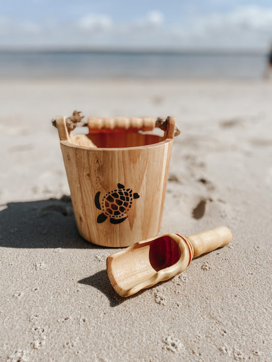 Wooden sand pail and shovel with turtle design on a sandy beach.