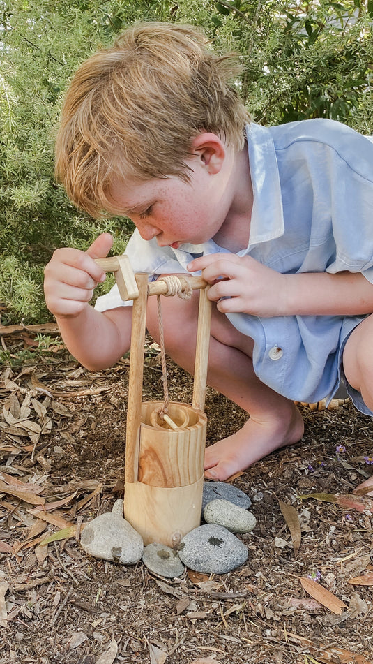 Child playing with a wooden toy outdoors on a natural ground.