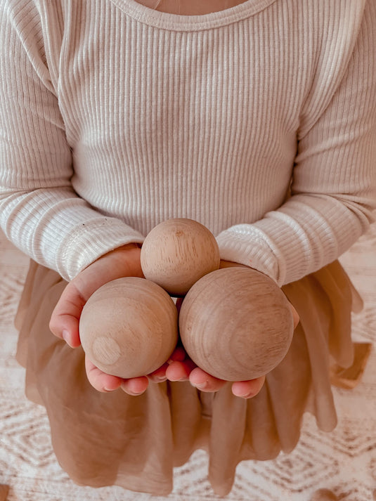 Person holding three wooden balls against a neutral background