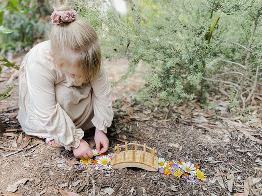 Child arranging flowers near a small wooden bridge in a natural setting