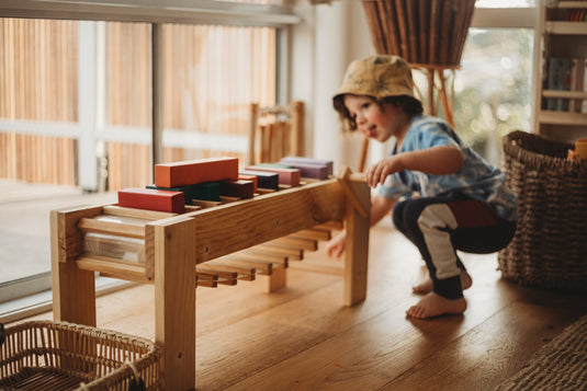 Child playing with wooden toys on a wooden floor in a bright room.