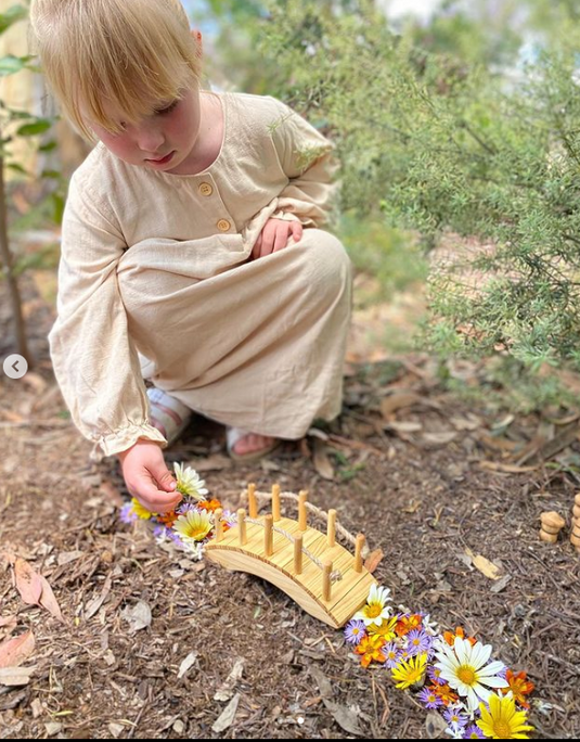 Child playing with a wooden bridge and flowers in a natural setting