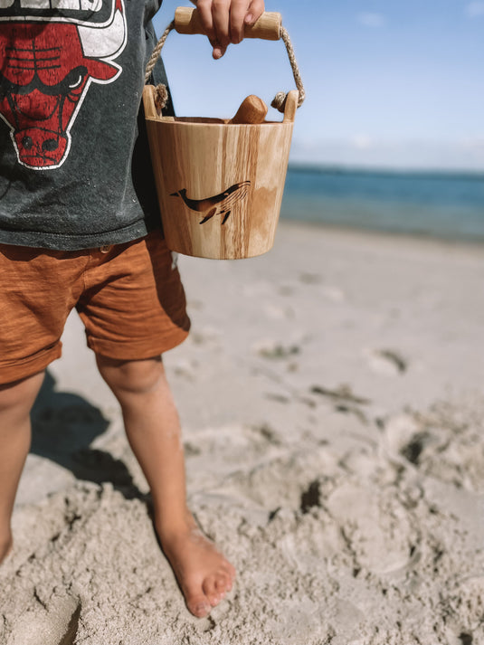 Child holding a wooden bucket on a sandy beach with ocean in the background