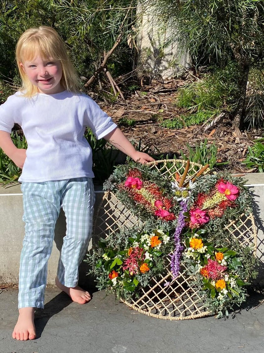 Child standing next to a decorative wreath with flowers and a dragonfly design outdoors.
