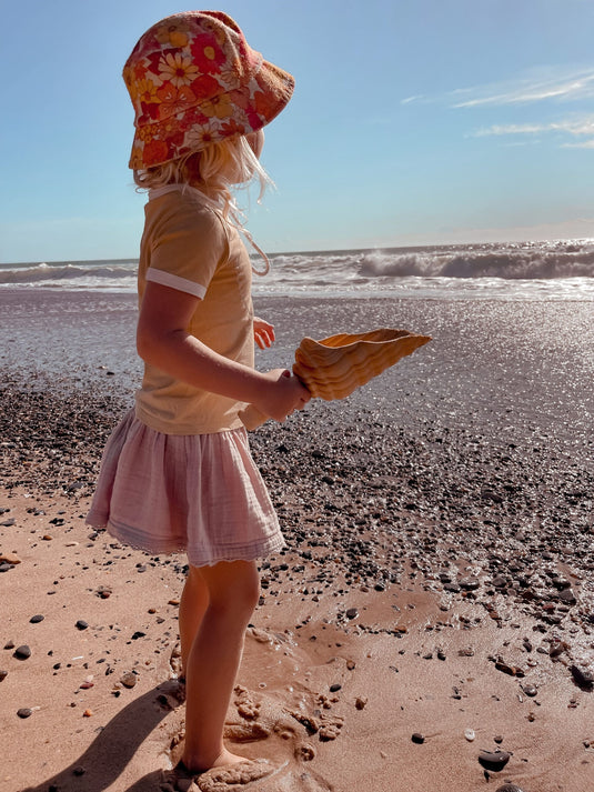 Child on a beach wearing a sun hat and holding a shovel