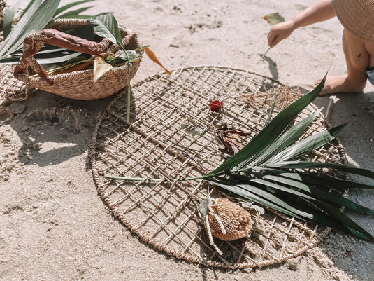 Woven mat on sandy ground with a basket and leaves