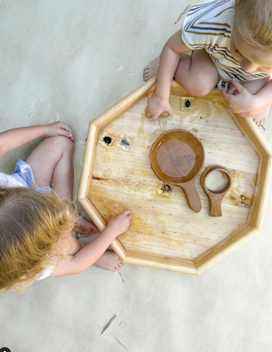 Two children playing with wooden toys on a hexagonal wooden tray.