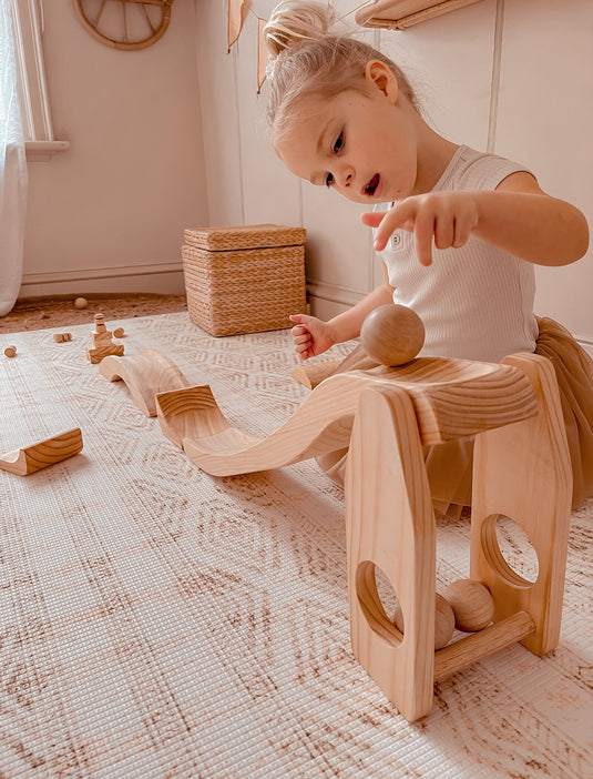 Child playing with wooden ball run on a patterned rug