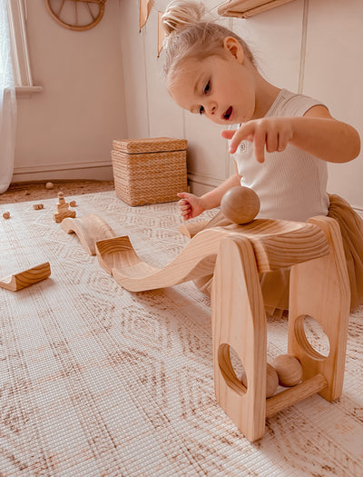 Child playing with wooden ball run on a patterned rug