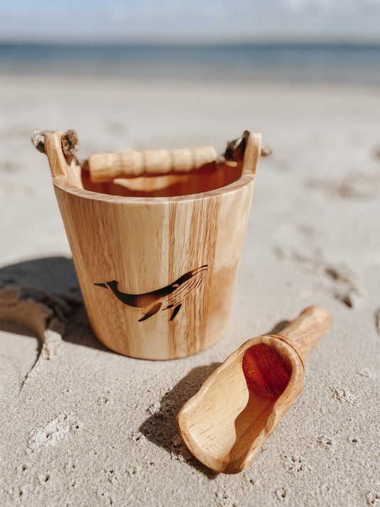 Wooden bucket and scoop on a sandy beach with ocean in the background