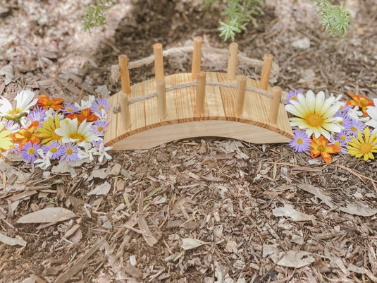 Miniature wooden bridge surrounded by colorful flowers on a natural ground surface